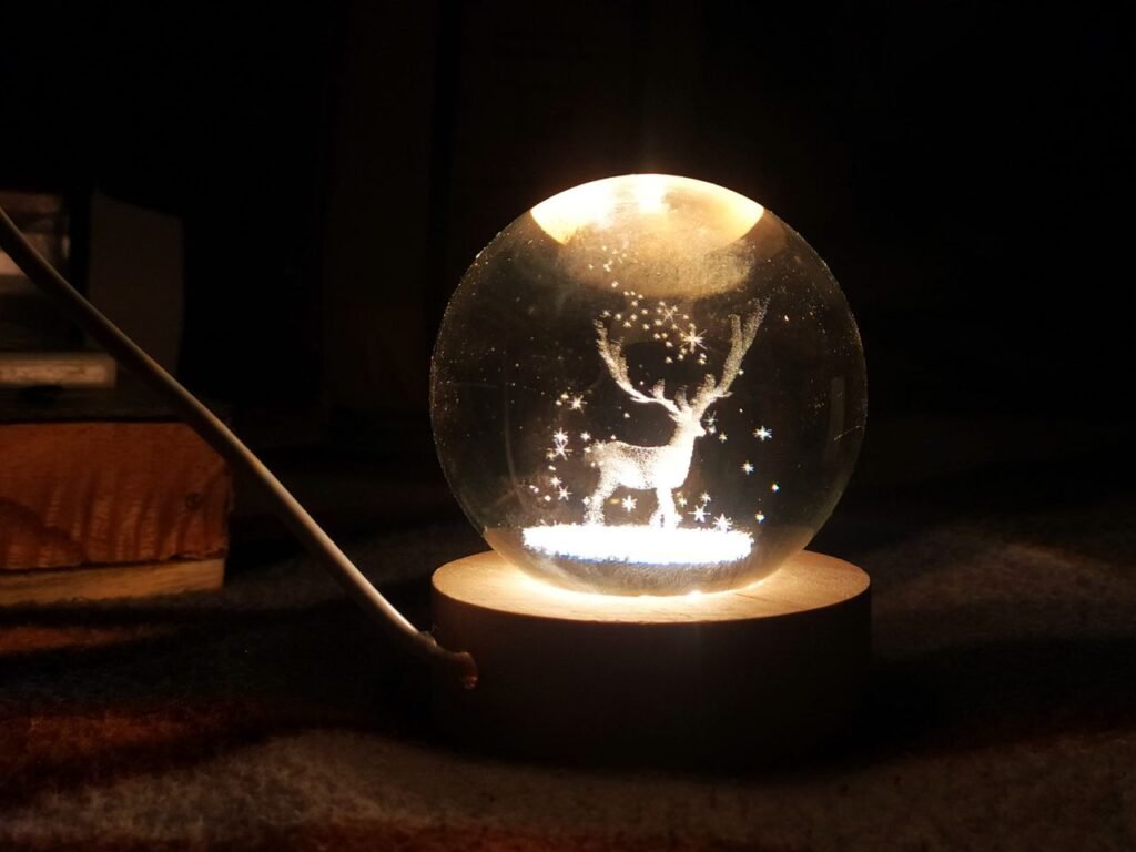 A beautifully lit snow globe featuring a deer and stars on a wooden base.