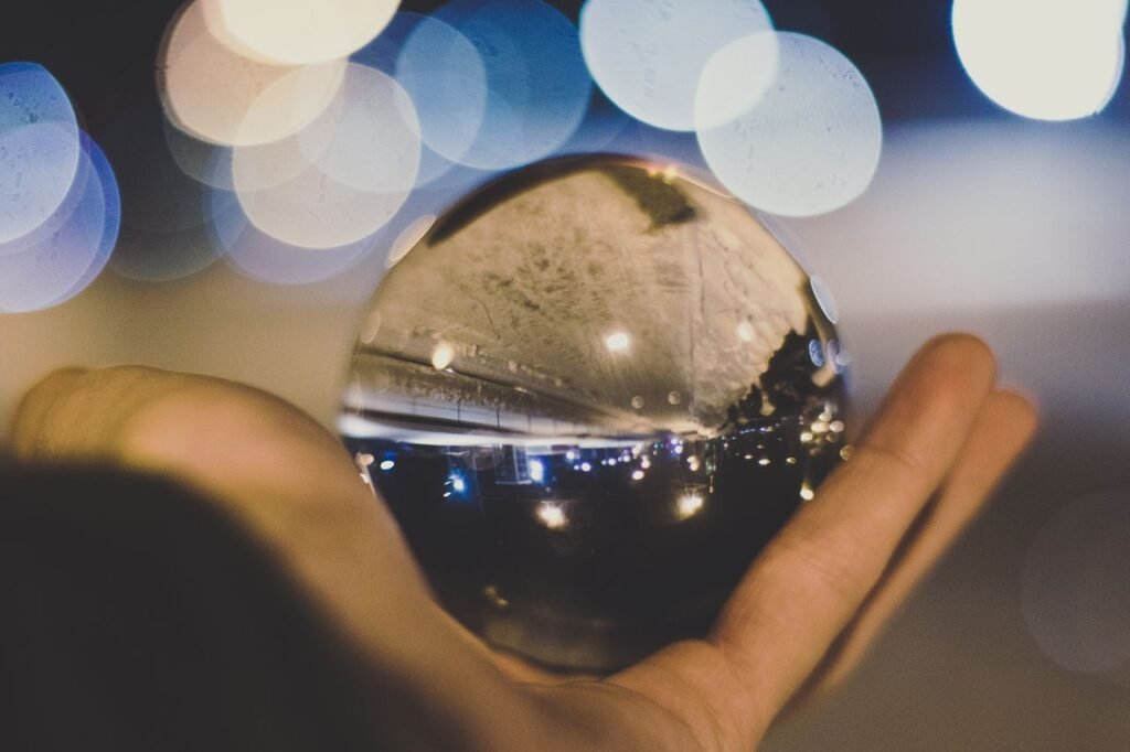 A crystal ball reflecting a street scene and lights, held in a hand against a blurred bokeh background.